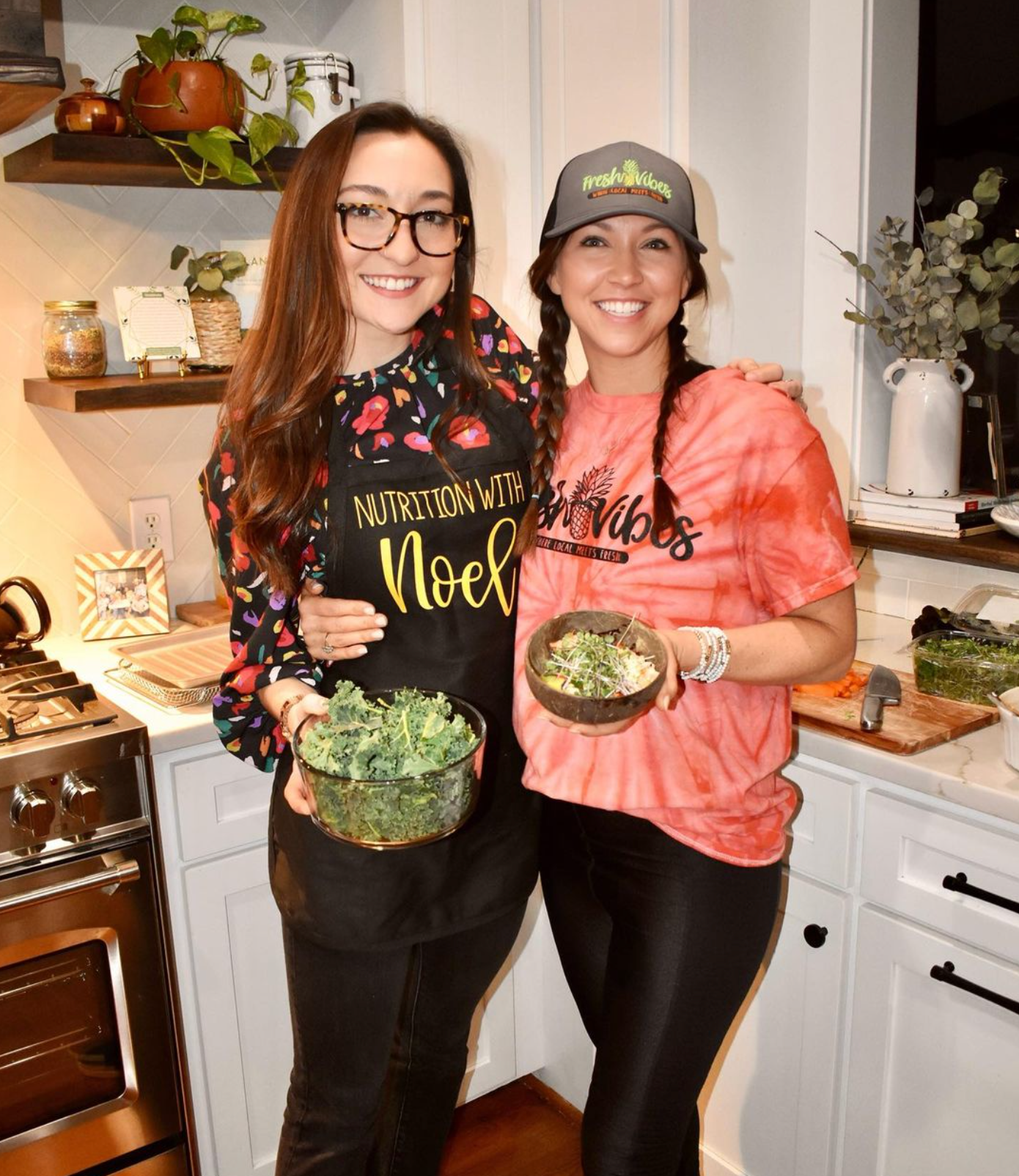 Two women are standing next to each other in a kitchen holding bowls of food.