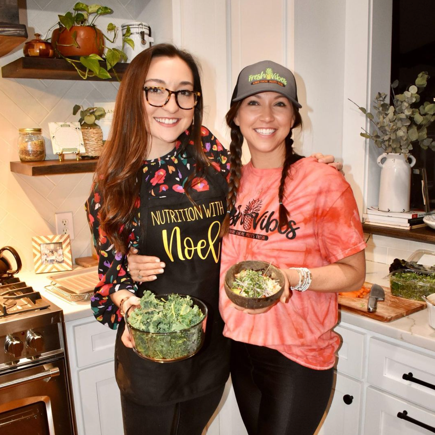 Two women are standing next to each other in a kitchen holding bowls of food.