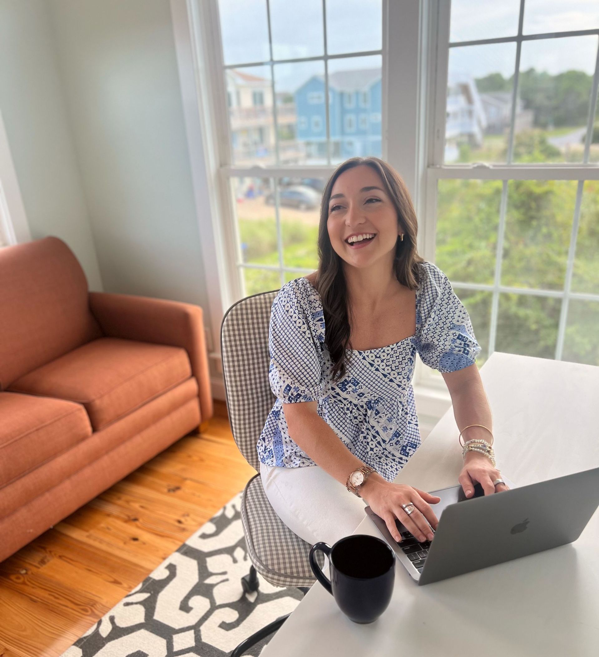 A woman is laughing while typing on her laptop