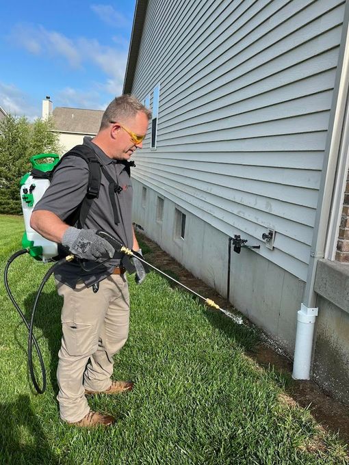 A man is spraying a house with a backpack sprayer.