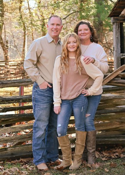 A family is posing for a picture in front of a wooden fence.