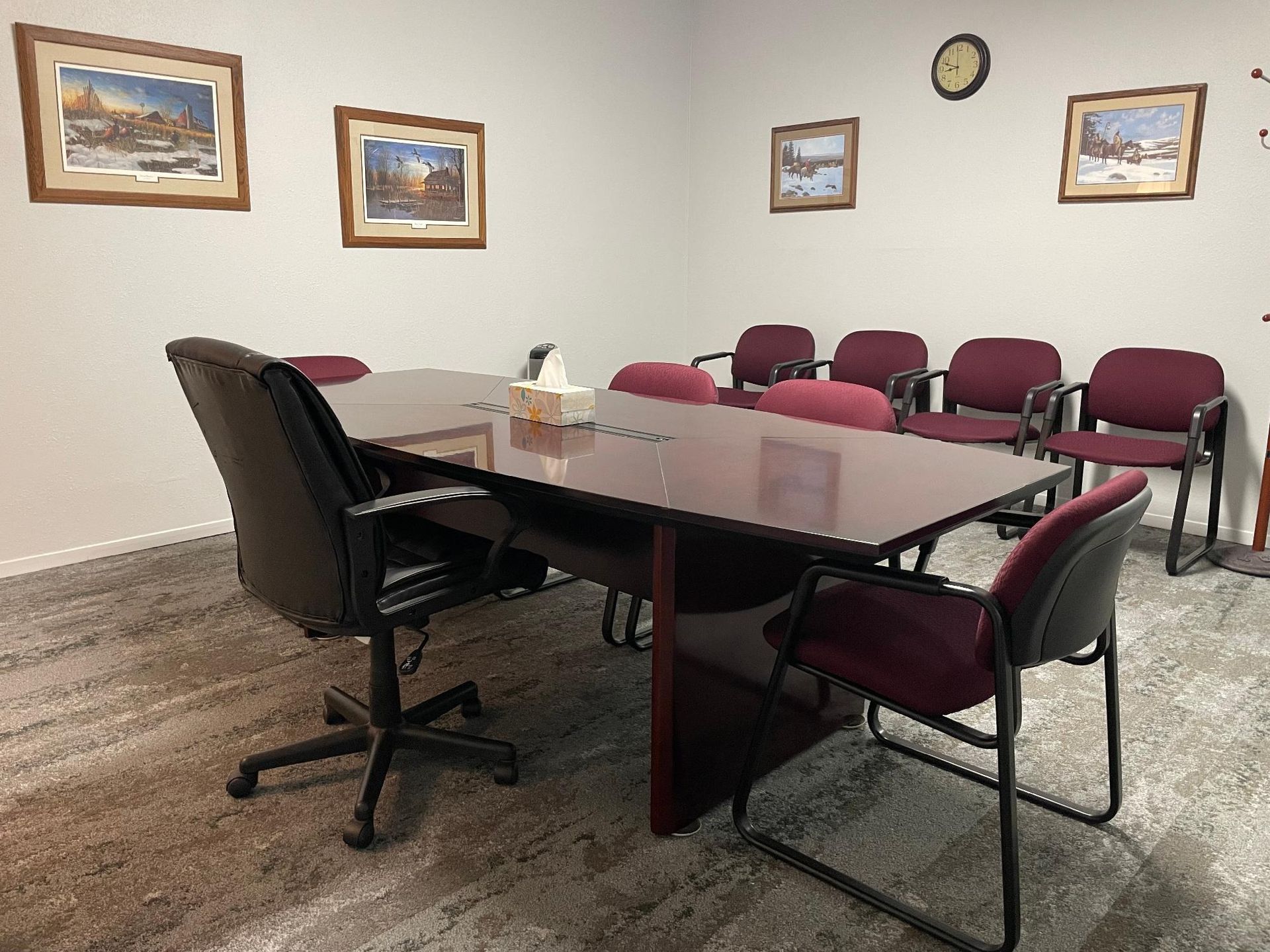 Conference room with dark wood table, burgundy chairs, artwork, and an office chair.