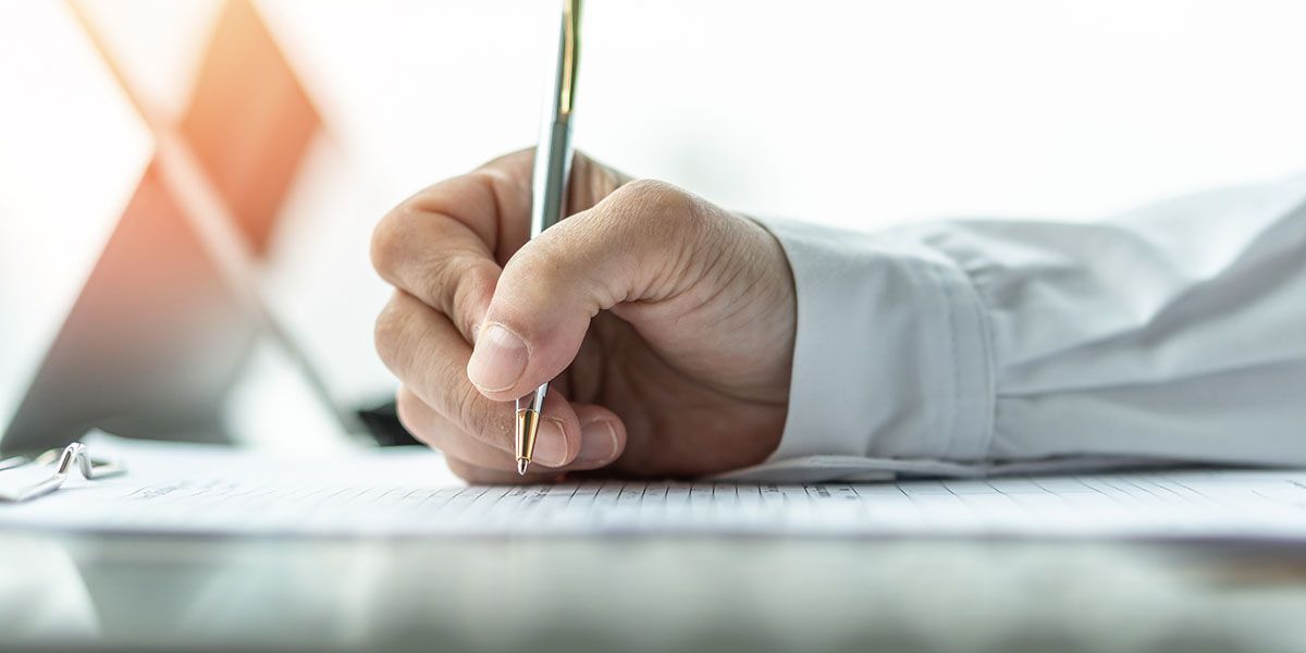 Person writing with a pen on a document, close-up shot of hand and paper.