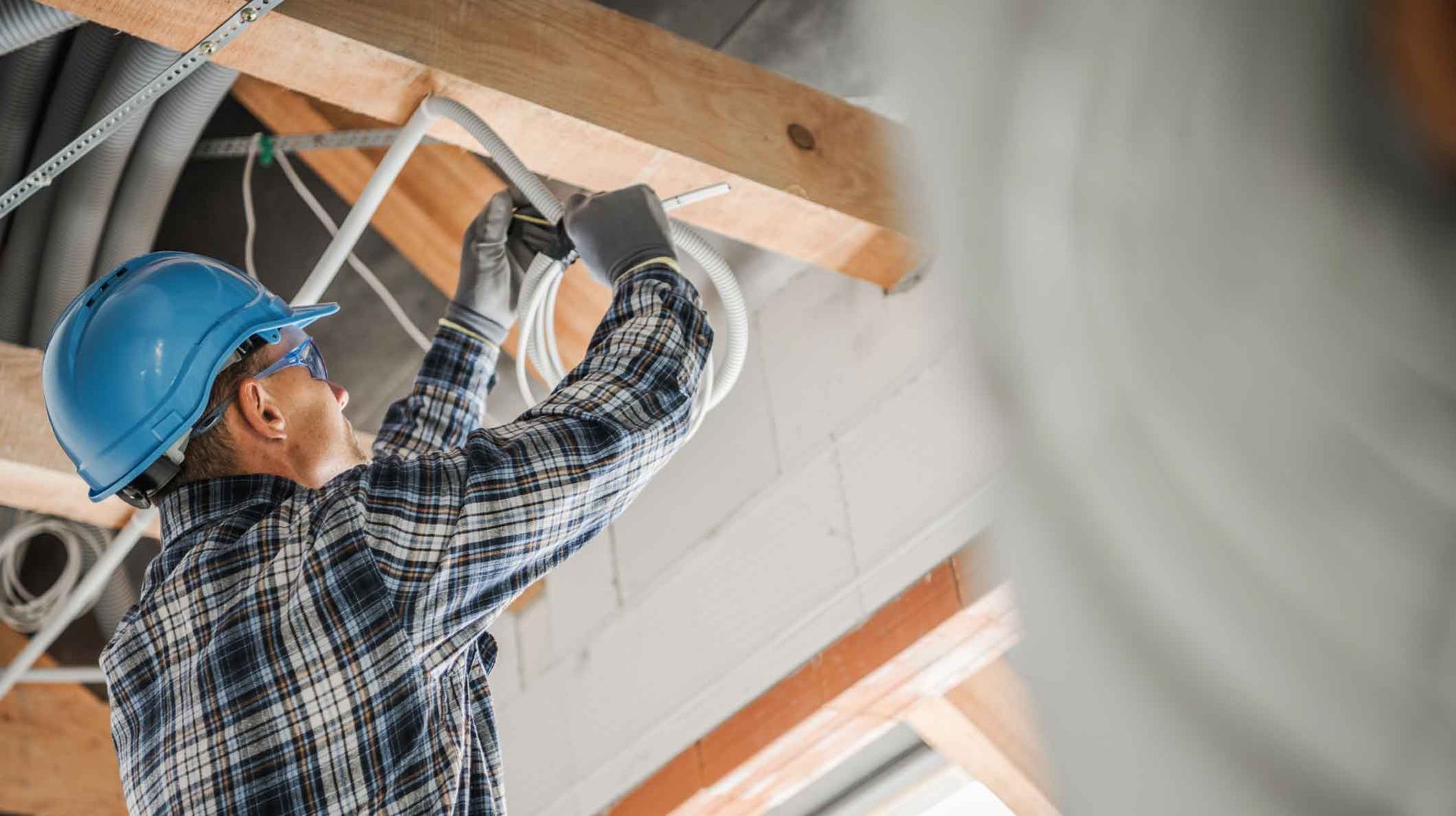 Construction worker in blue hard hat installing ceiling framing indoors