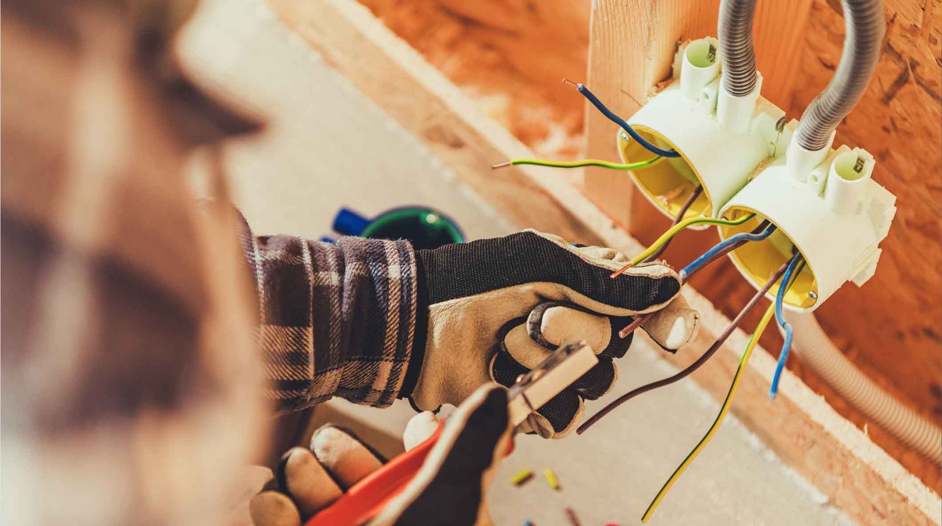 Electrician wiring a wall outlet with pliers and red-handled cutters near exposed colored wires