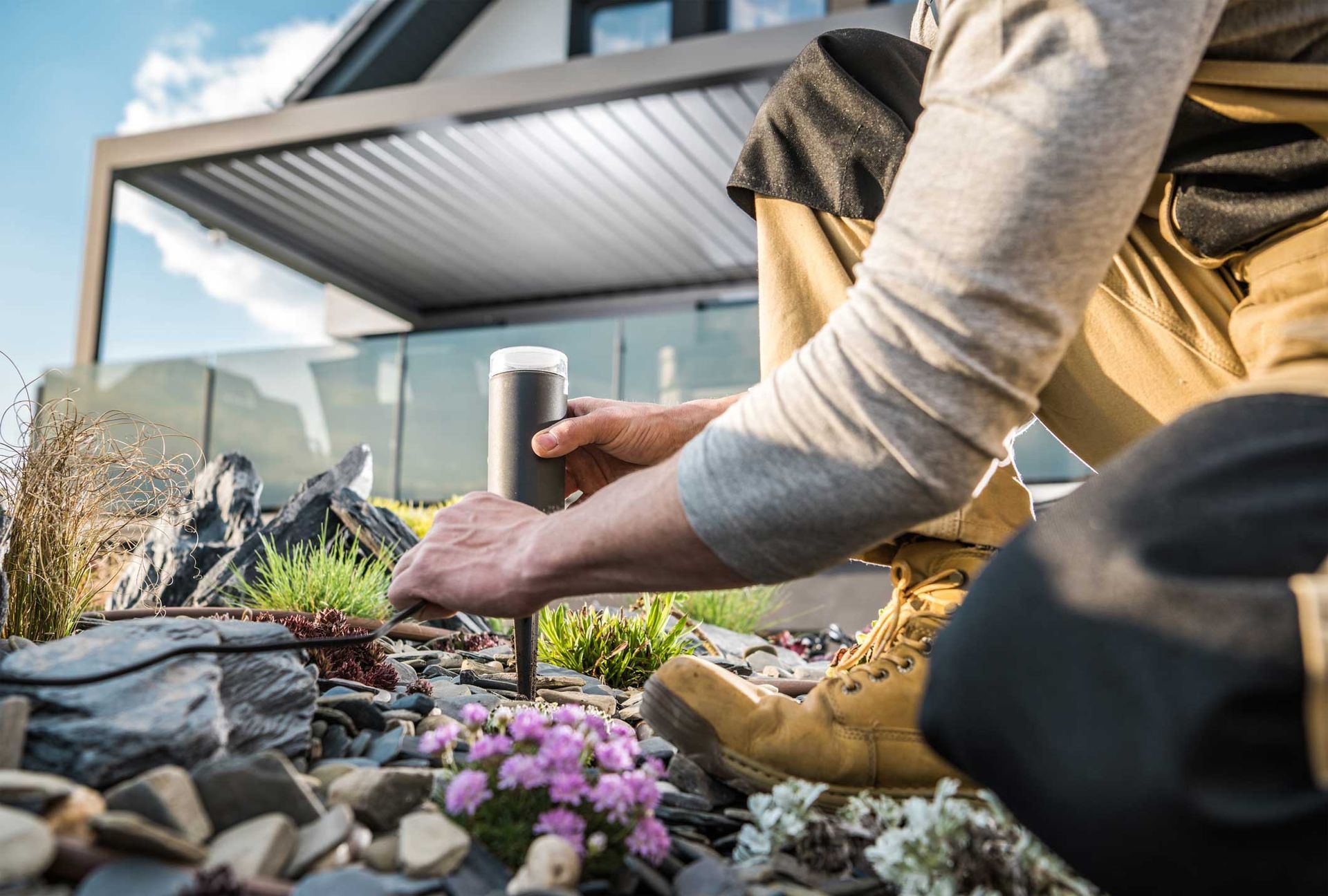 Person planting flowers in a raised garden bed beside a house patio