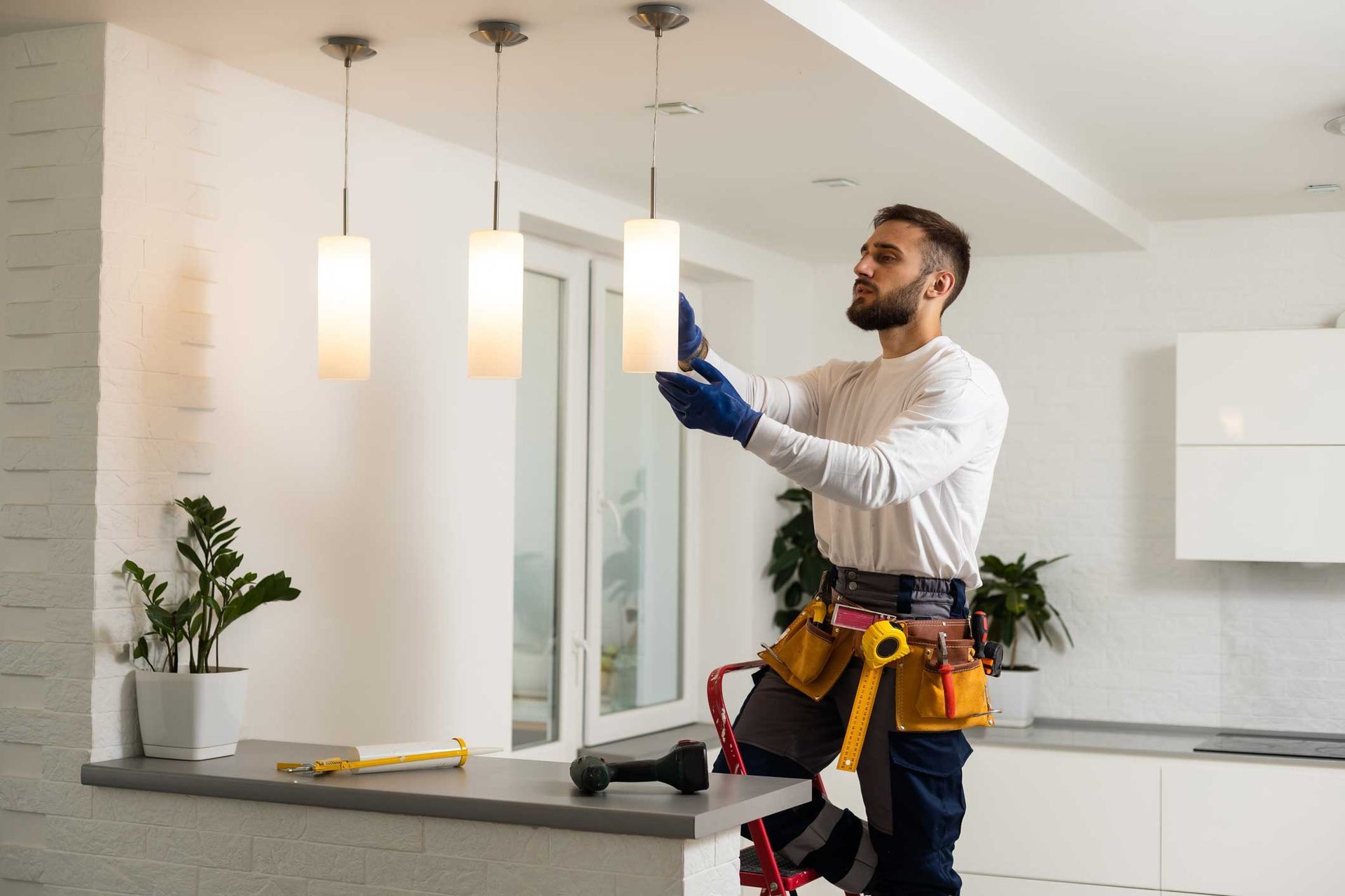 Electrical lighting contractor installing modern pendant lights in a residential kitchen.