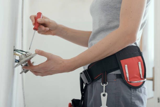 Electrician installing wall electrical outlet with screwdriver, wearing tool belt renovation indoor.