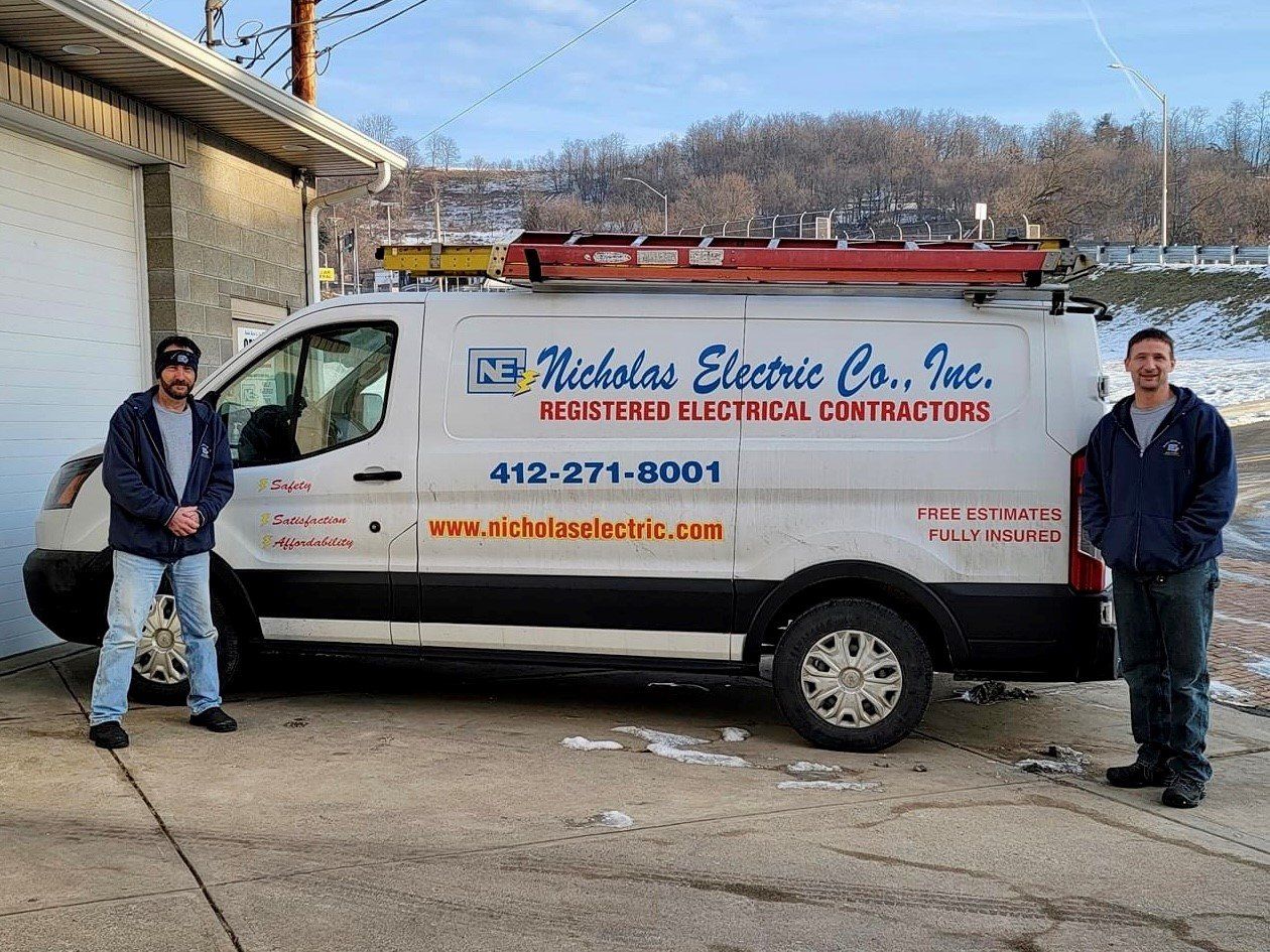 An electrical service van parked outdoors with two people standing beside it near a garage building