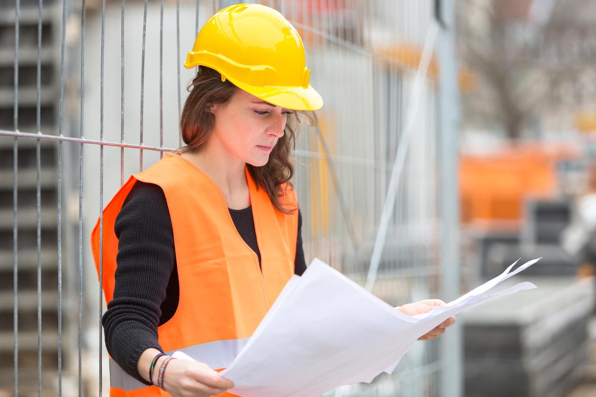 Construction worker in safety gear reviewing blueprints at active construction site.