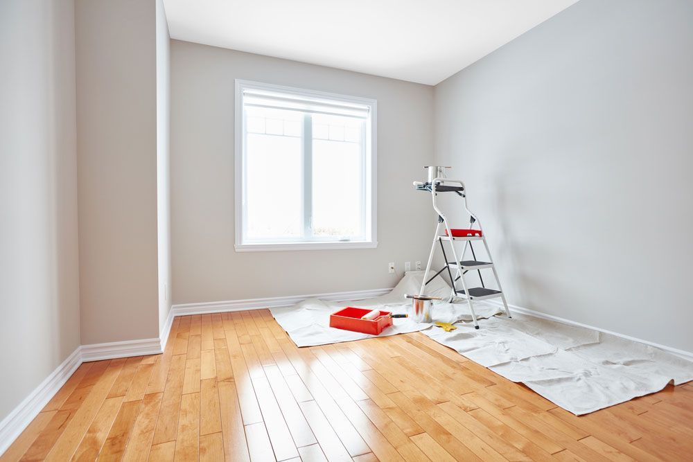 An empty room with hardwood floors and white walls is being painted.