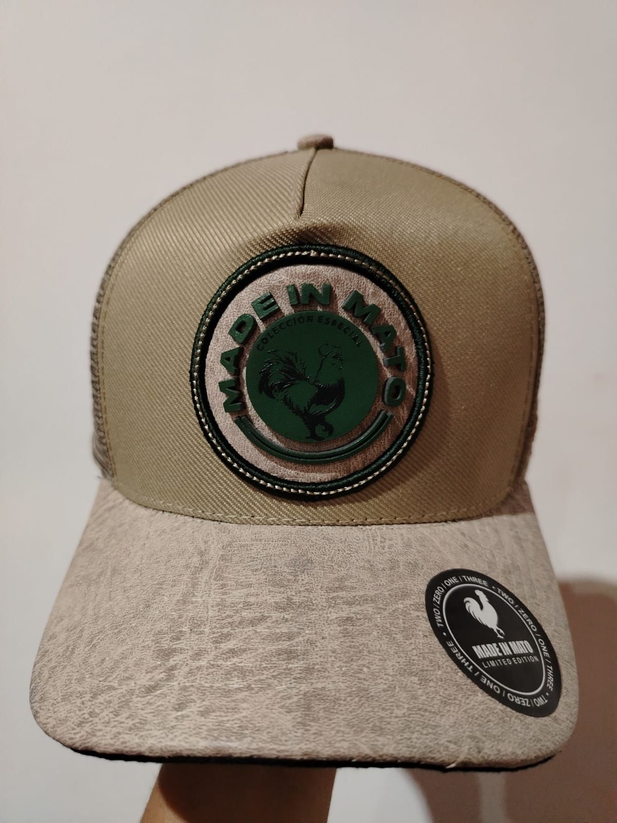 Gorra de camionero color canela con un parche circular verde y blanco que dice "MADE IN MEIO".