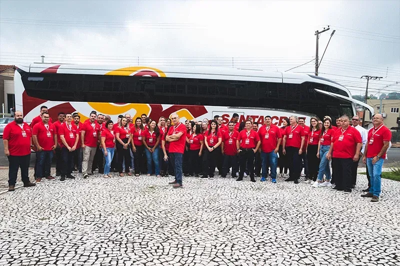 Um grande grupo de pessoas está posando para uma foto em frente a um ônibus.