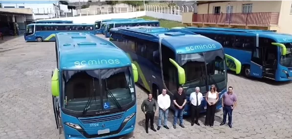 Um grupo de pessoas em pé na frente de uma fileira de ônibus azuis.