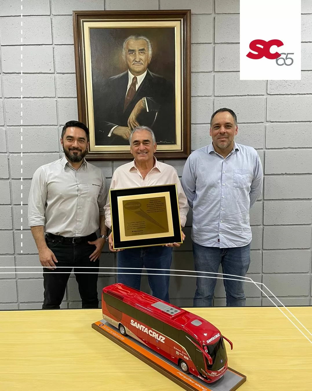 Três homens estão de pé ao lado de uma maquete de ônibus.