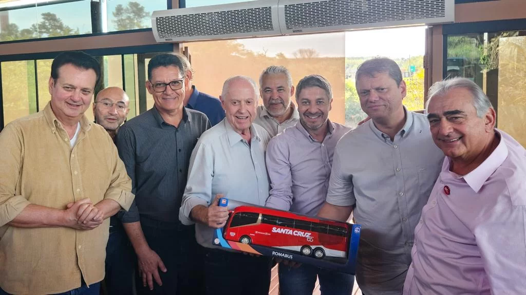 Um grupo de homens está posando para uma foto enquanto segura uma maquete de um ônibus.