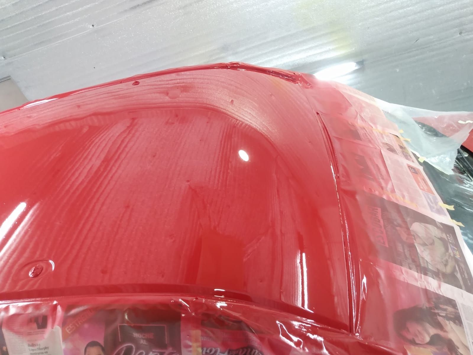 Pieza de coche roja siendo pintada en un taller, con rayas de pintura húmeda visibles.