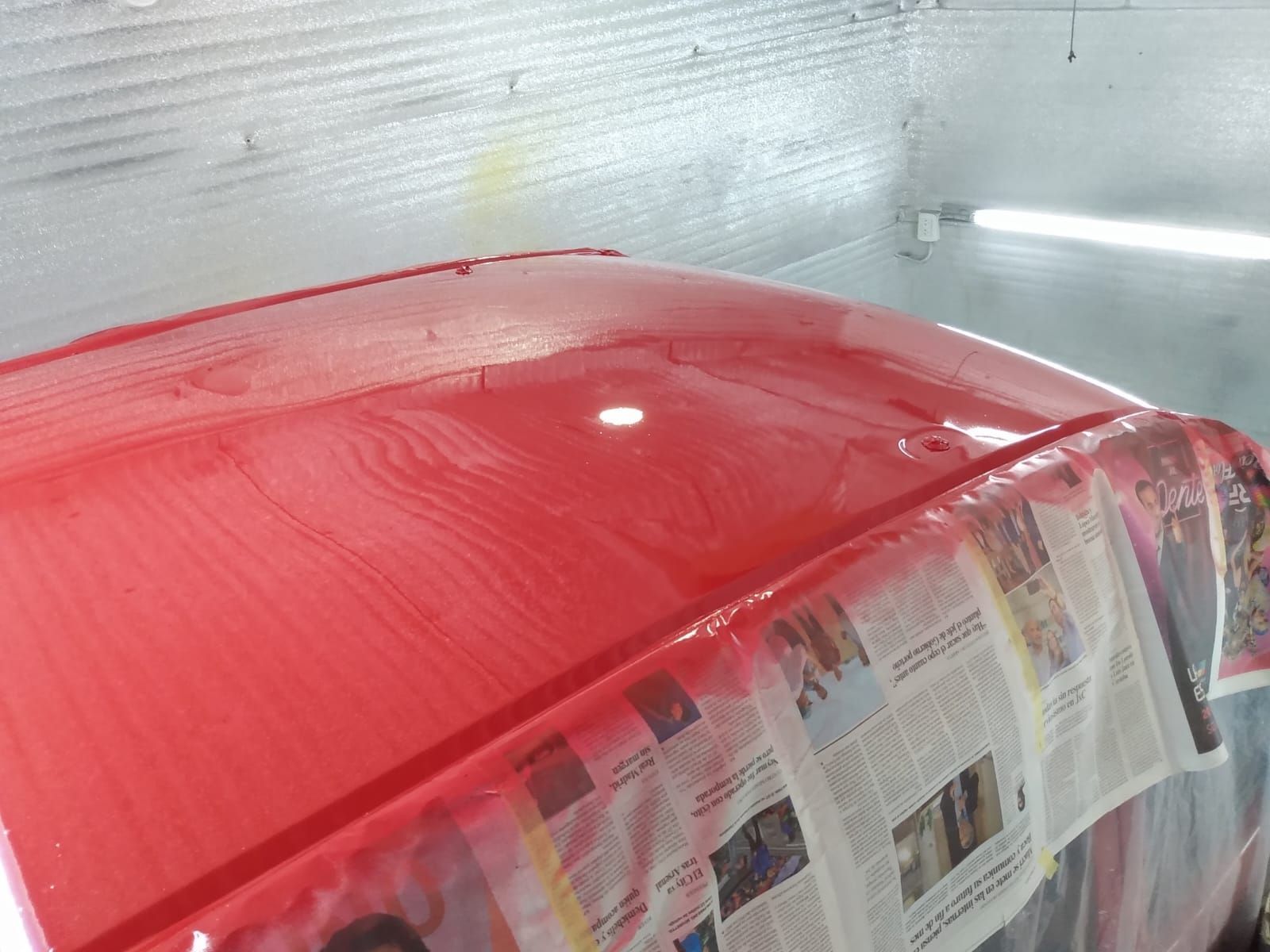 Techo de coche rojo pintado en cabina de pintura, cubierto con papel de periódico.