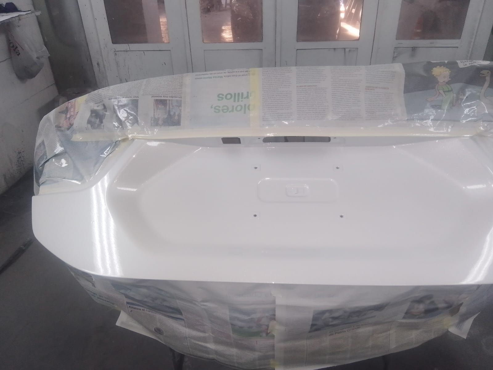 Tapa de maletero de coche de color blanco, tapada con papel de periódico, preparada para pintar en taller.