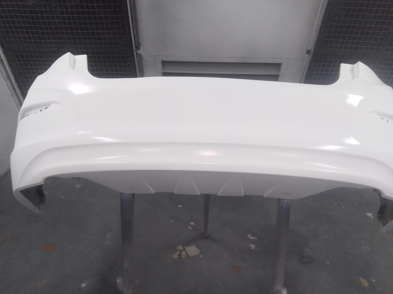 Parachoques de coche de color blanco, recién pintado, montado en cabina de pintura.