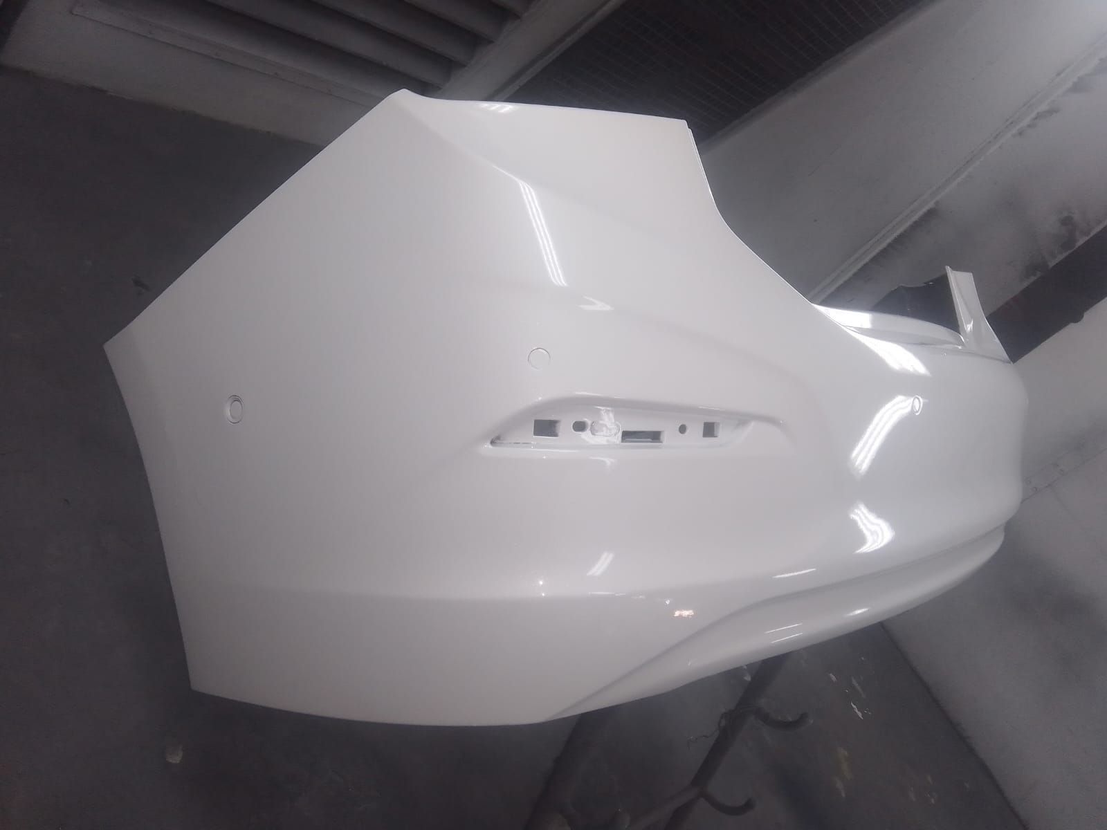 Parachoques de coche de color blanco, recién pintado, en el interior de un taller.