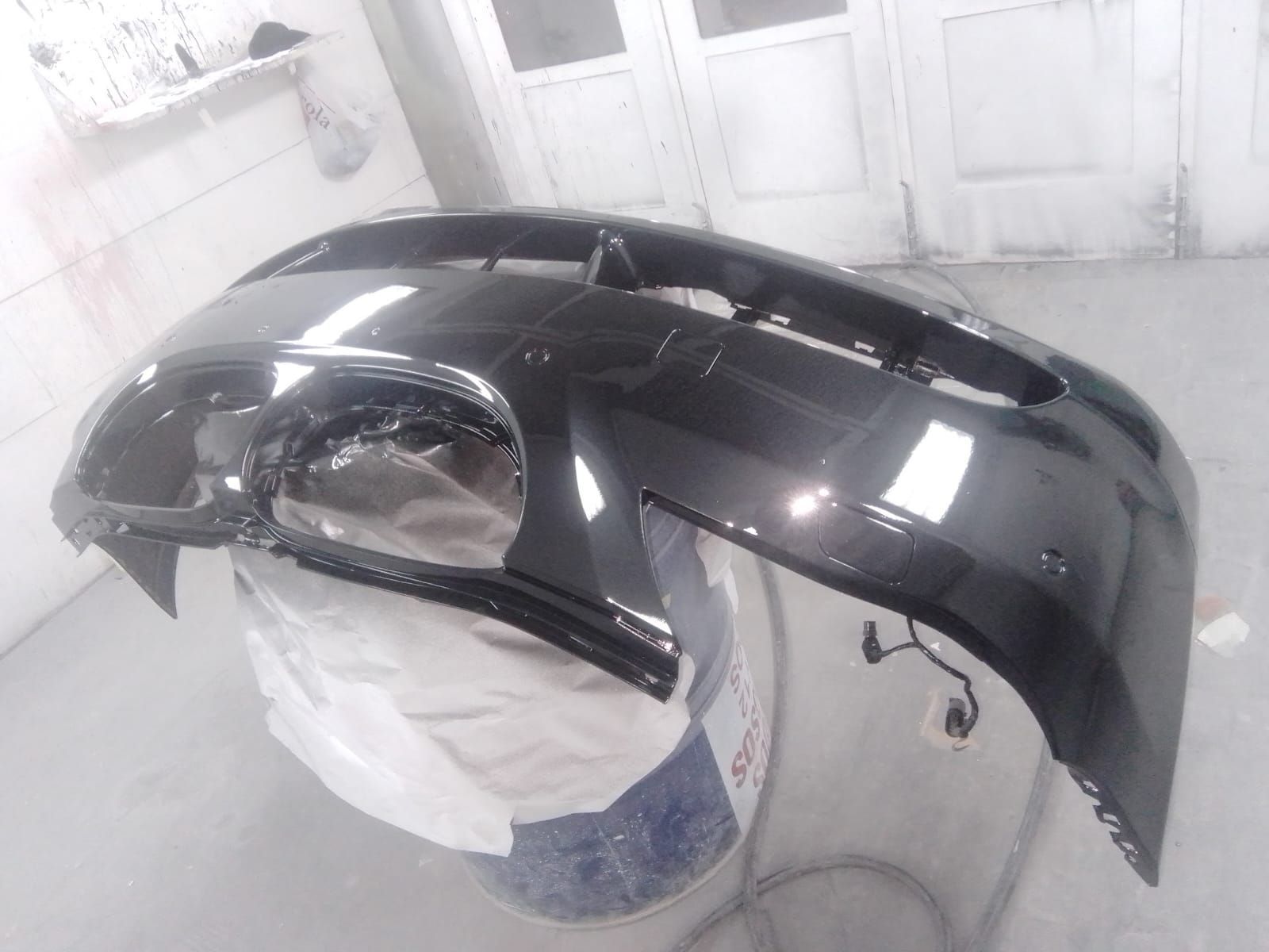 Parachoques de coche negro, recién pintado y brillante, apoyado sobre un cubo en un taller.