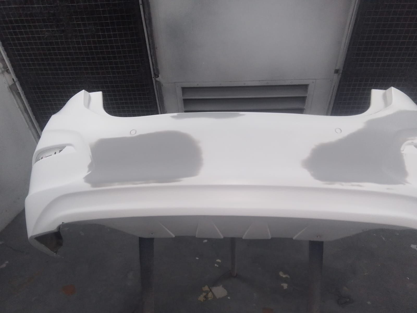 Parachoques de coche blanco en cabina de pintura, con manchas grises, listo para pintar.