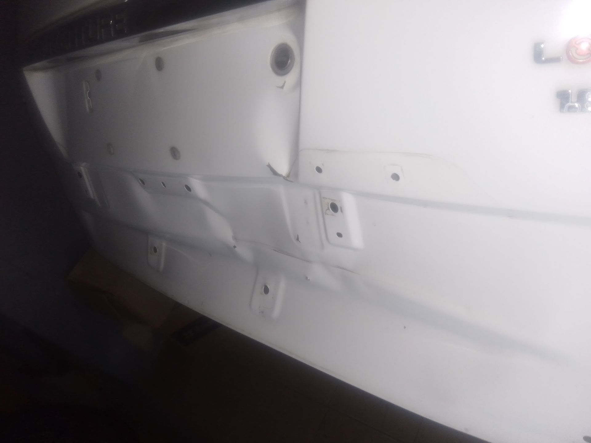 Parachoques de coche blanco con abolladuras y daños.