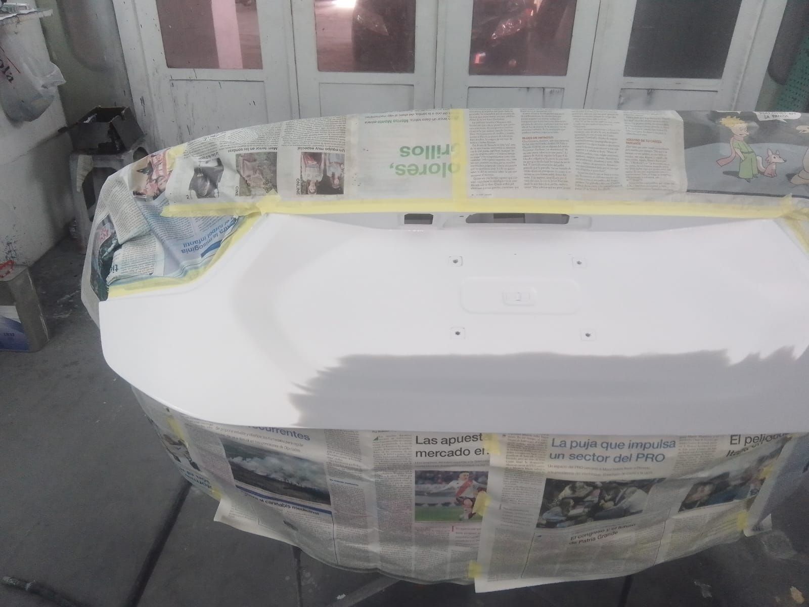 Baúl de auto blanco preparado para pintar, papel de periódico cubriendo área alrededor de un garaje.