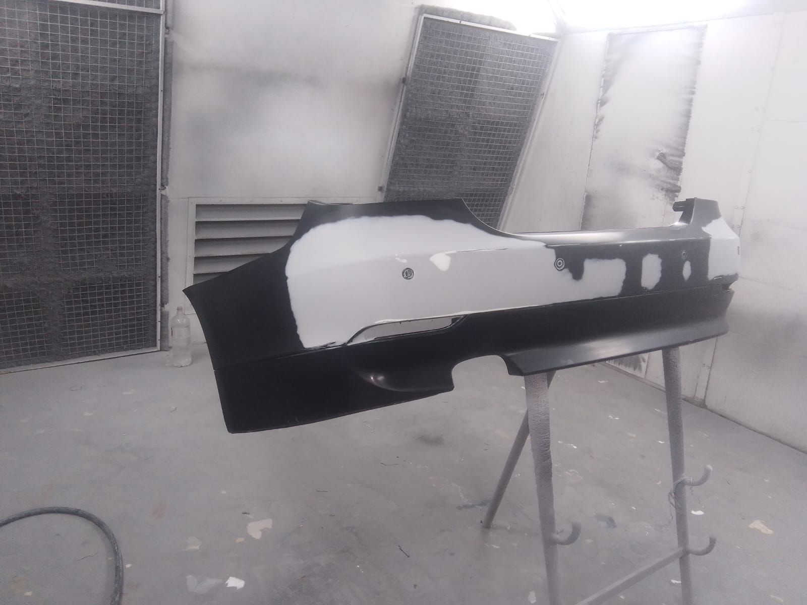 Parachoques de coche negro pintado de gris en una cabina de pintura.