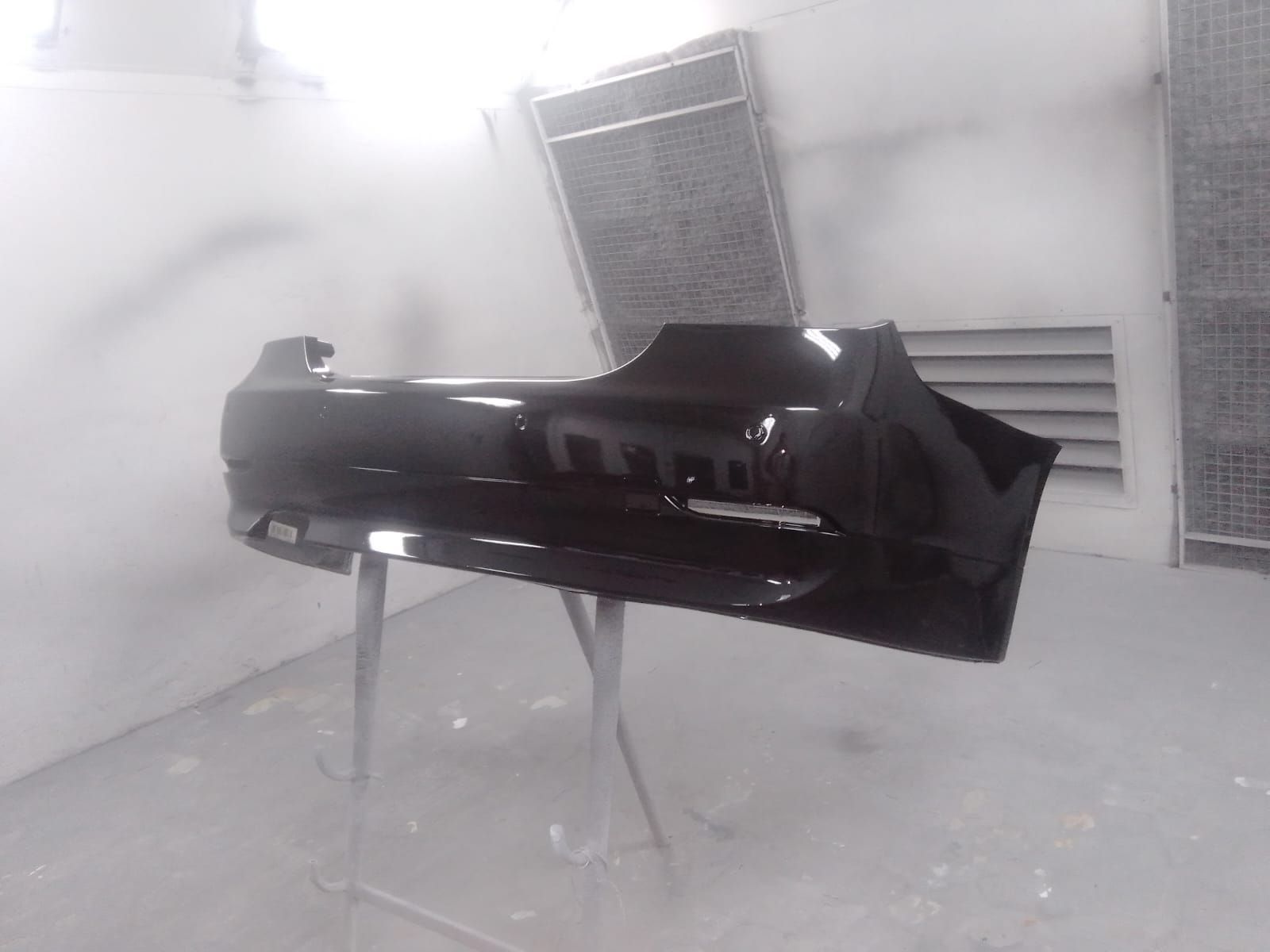 Parachoques de coche negro, recién pintado, sobre un soporte en una cabina de pintura.