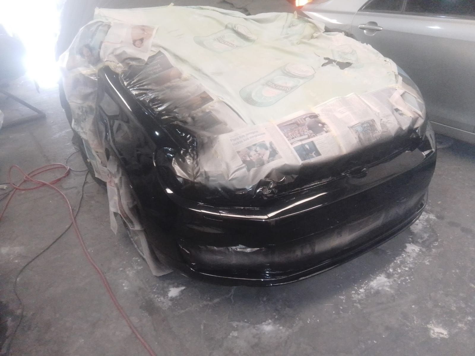 Parachoques de coche pintado de negro; áreas circundantes cubiertas de periódicos, en un garaje.