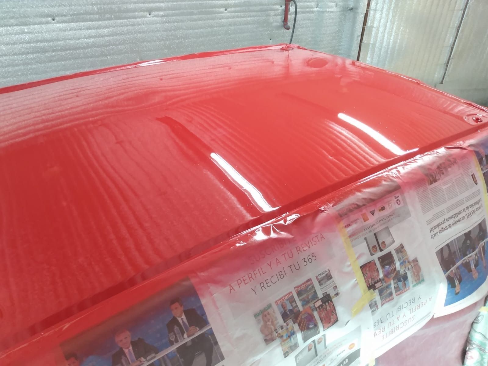 Techo de coche rojo con pintura brillante, papel de periódico protegiendo los bordes en una cabina de pintura.