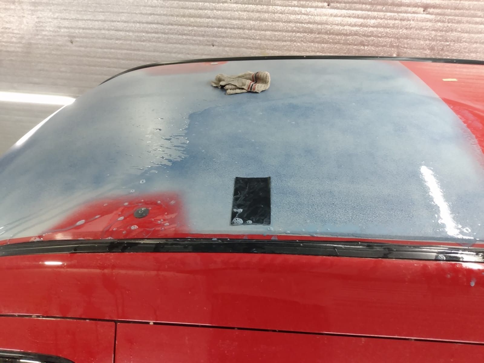 Techo de coche rojo con un parche azul grisáceo lijado, un panel rectangular negro y una tela encima.
