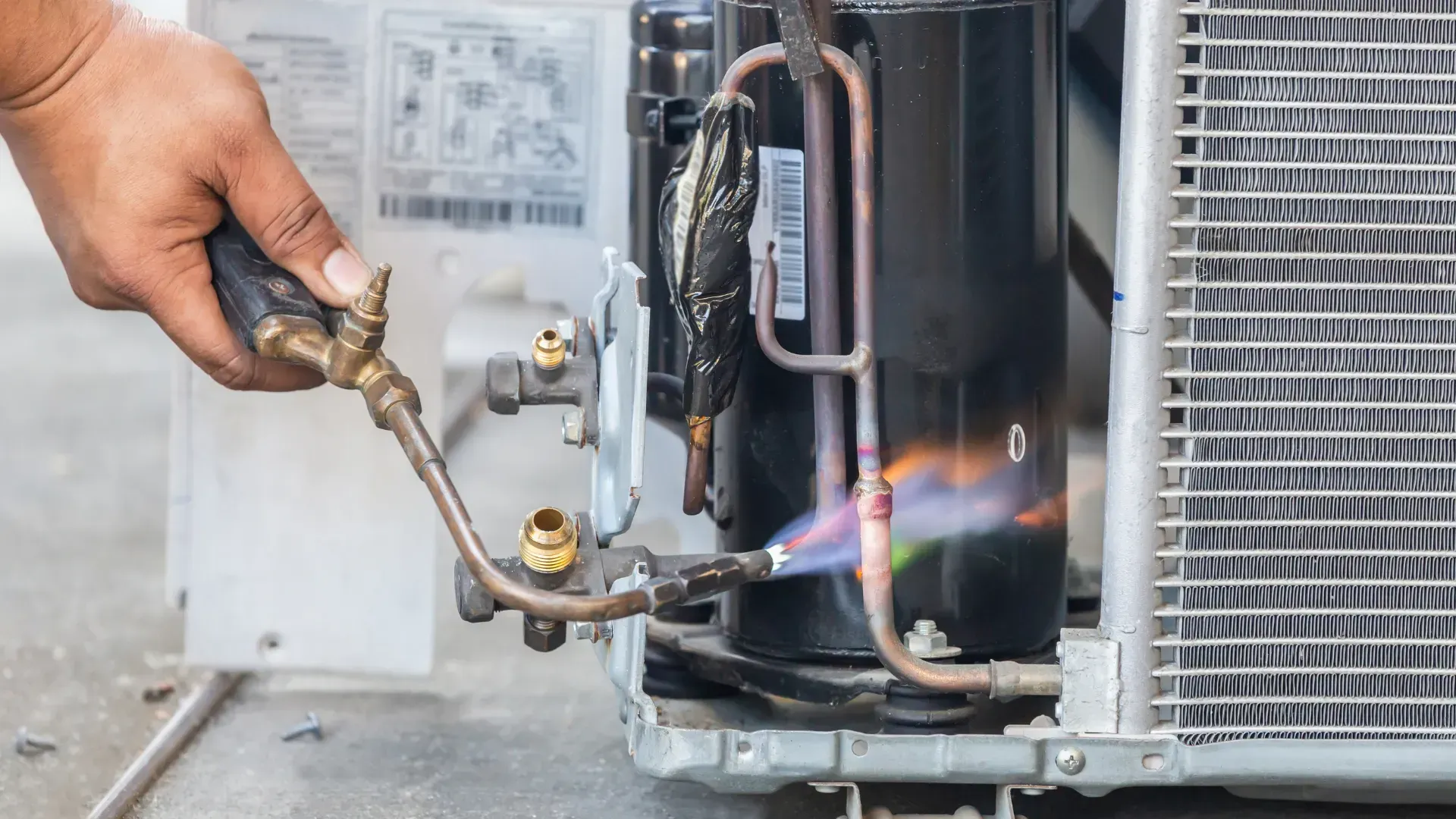 Hand welding copper tubes on an air conditioner, flame visible.