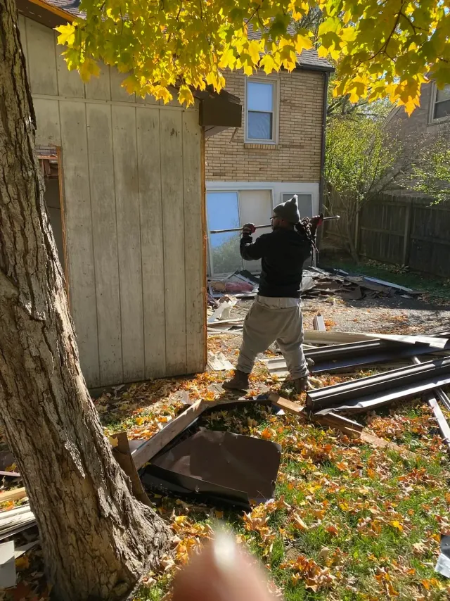 A man is standing in front of a house holding a hammer.