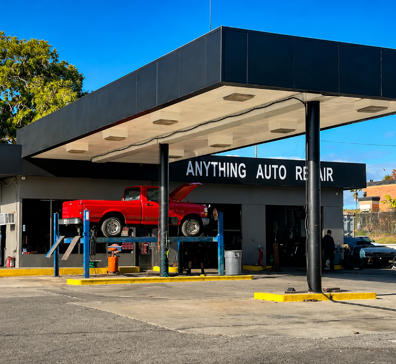 Red classic car on a lift at an auto repair shop with a dark canopy and “ANYTHING AUTO REPAIR” sign | Anything Auto Repair