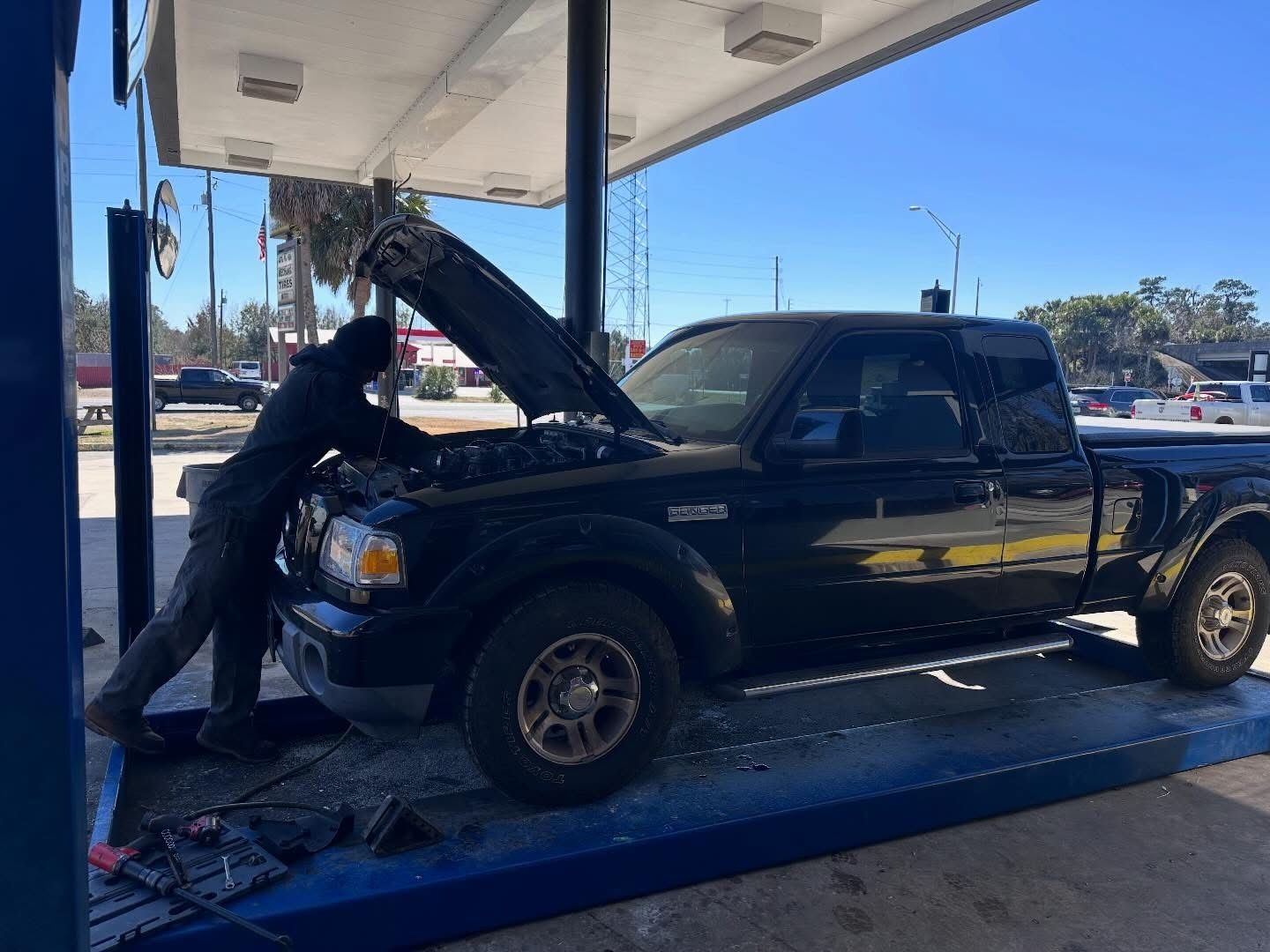 Person working on black pickup truck hood at a gas station under a canopy | Anything Auto Repair