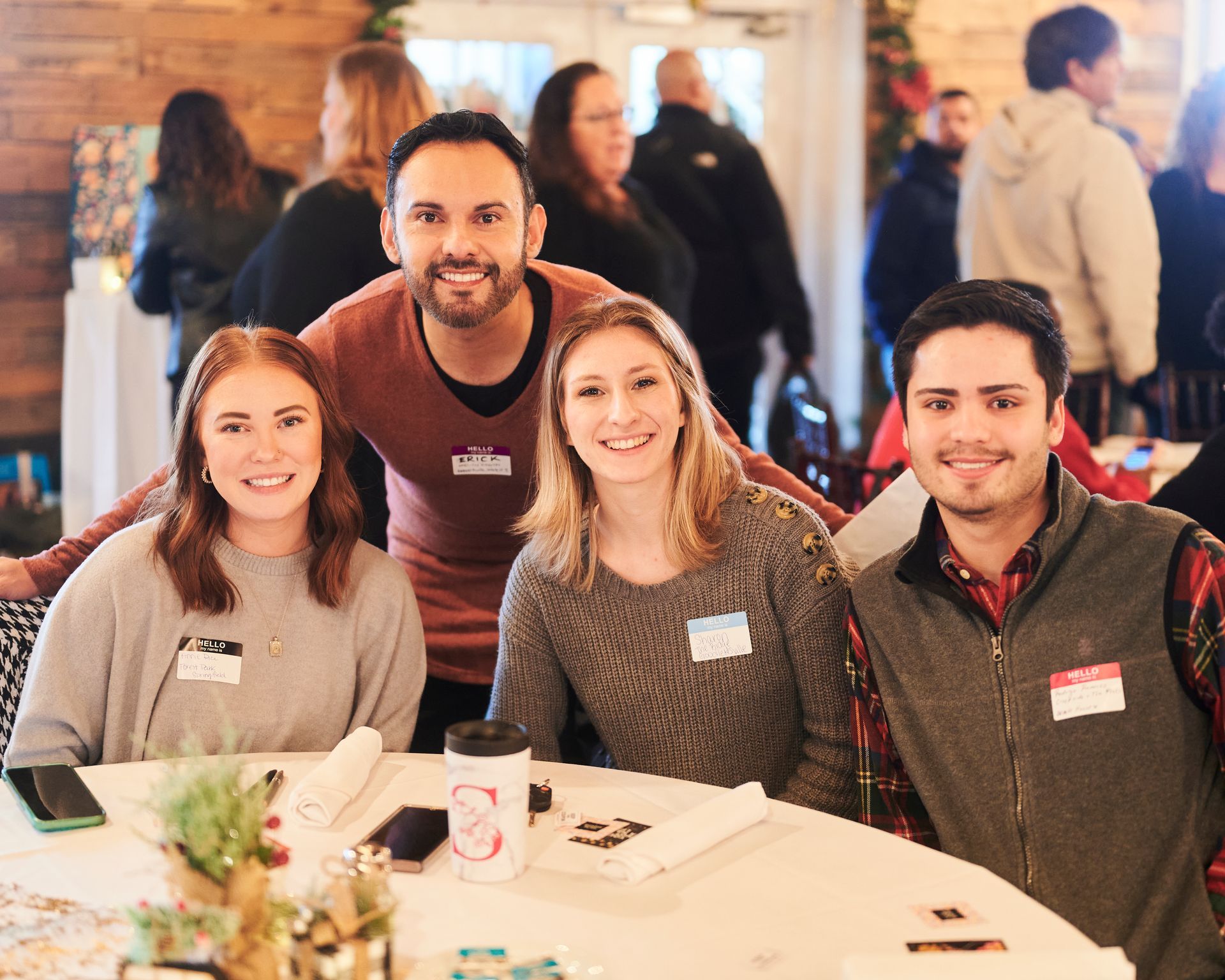 Four smiling people at a table, looking at the camera, inside a building with a holiday decor.