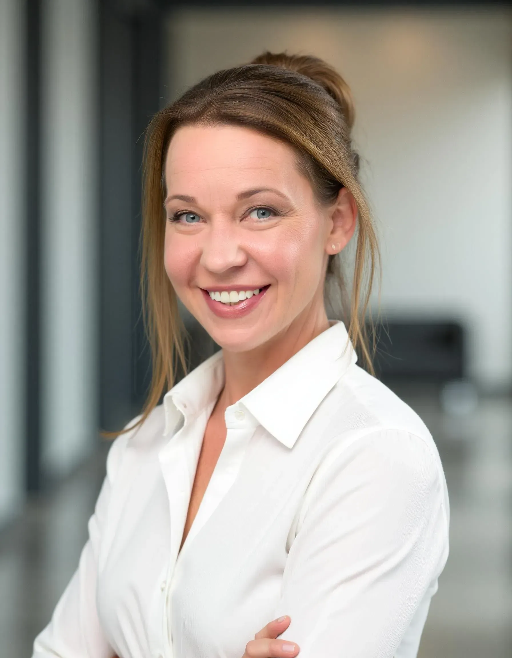 Woman in white shirt smiling at the camera in a modern building.