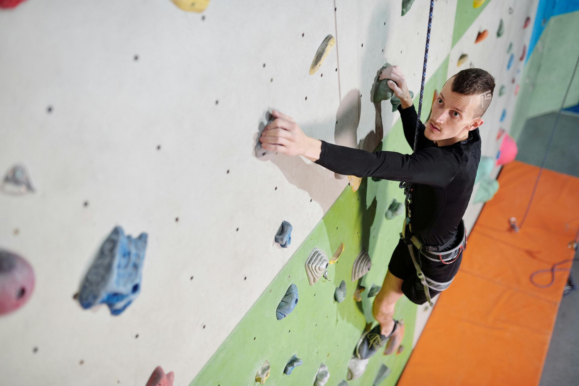 Man climbing a colorful indoor rock wall, reaching for holds with focused expression.