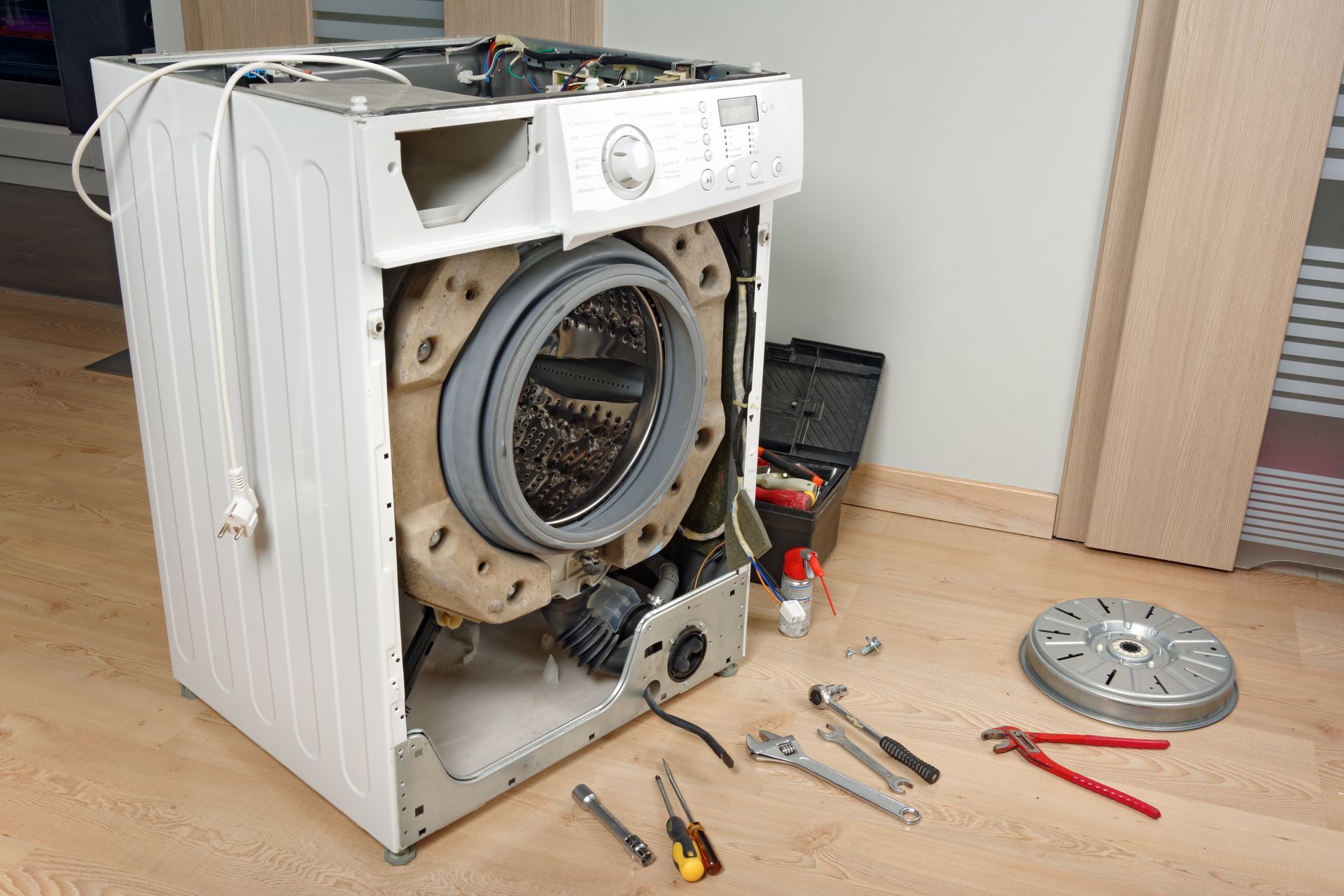 A washing machine is being repaired with tools on the floor.