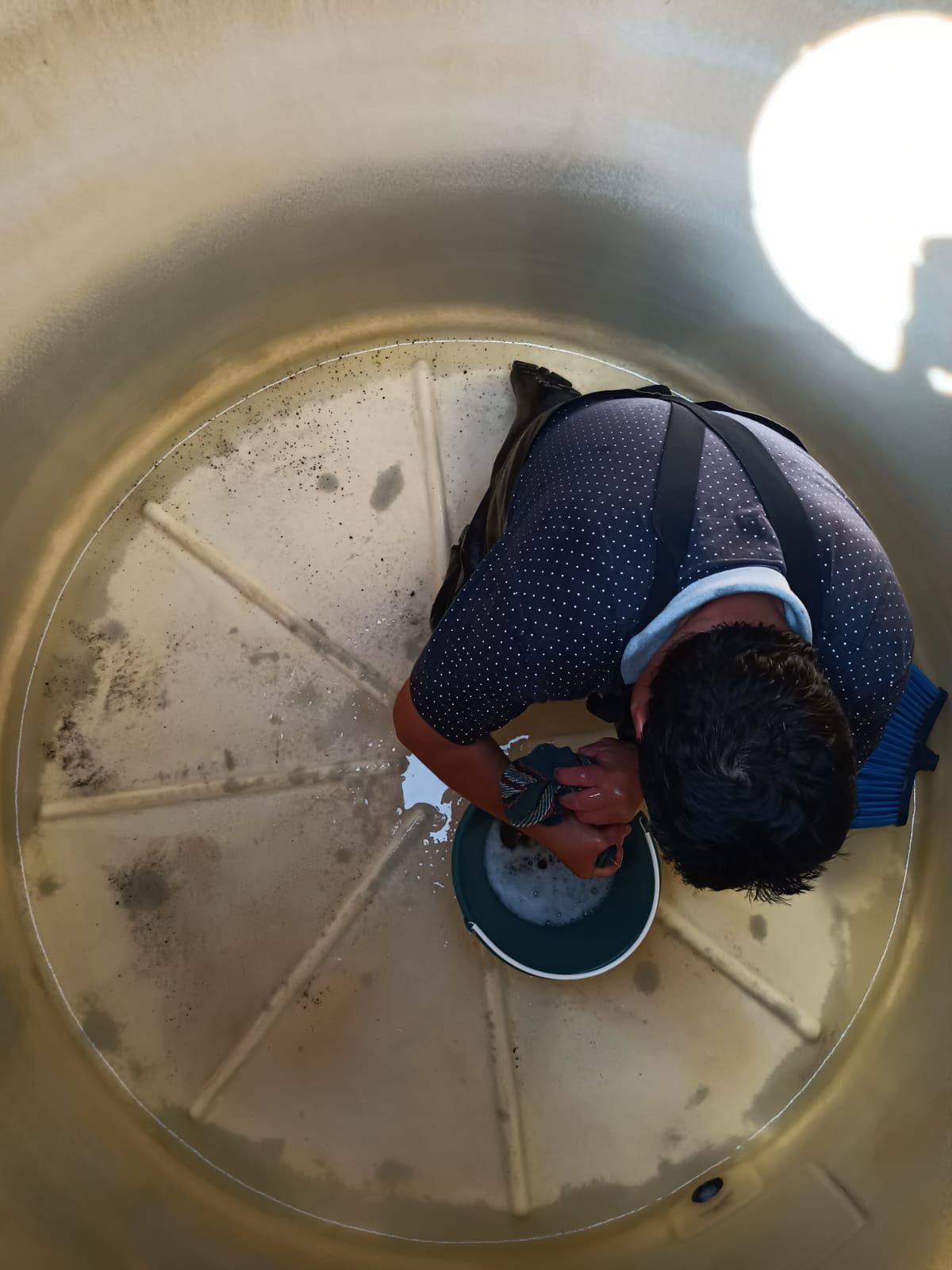 Persona limpiando el interior de un gran tanque de agua color beige.