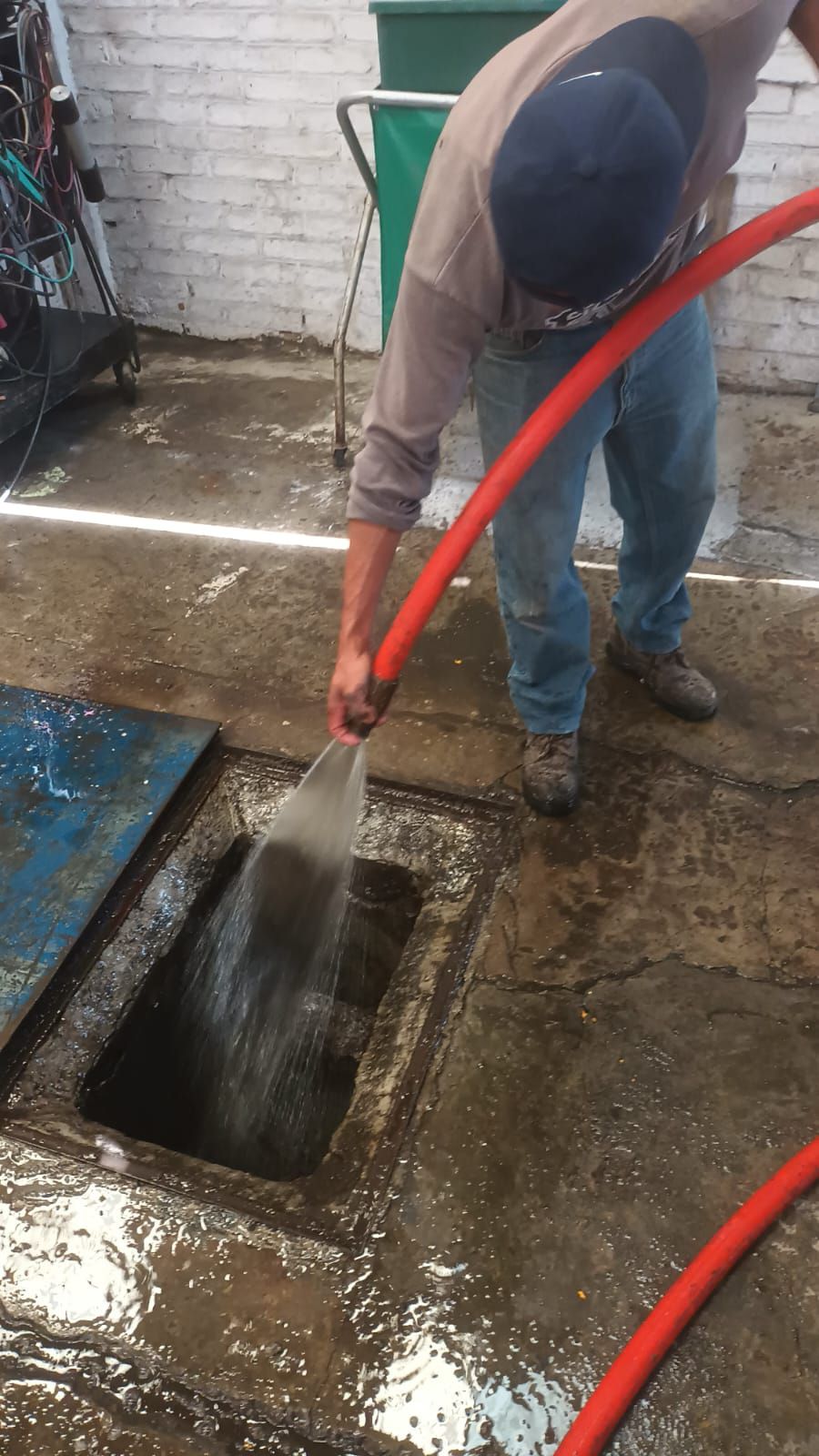 Persona utilizando una manguera para rociar agua en un desagüe abierto en una zona de hormigón.