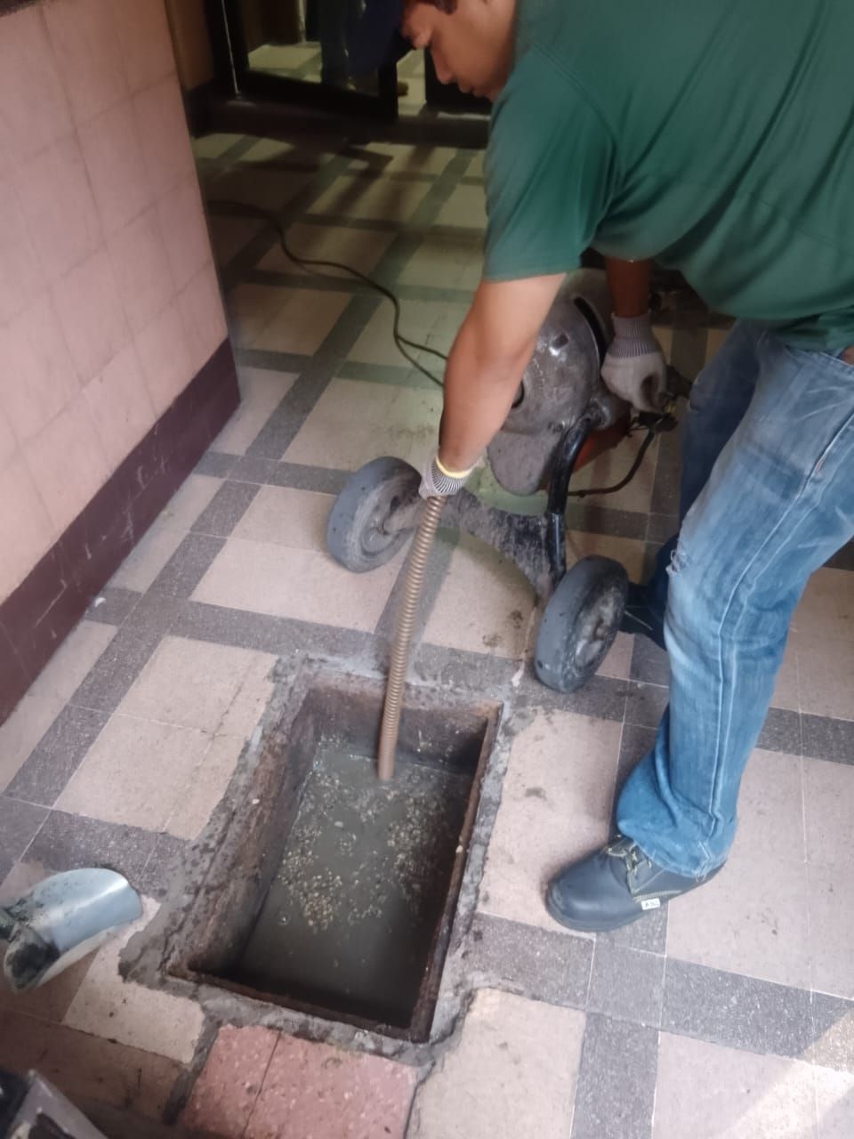 Hombre utilizando una herramienta desatascadora para limpiar un desagüe interior obstruido.