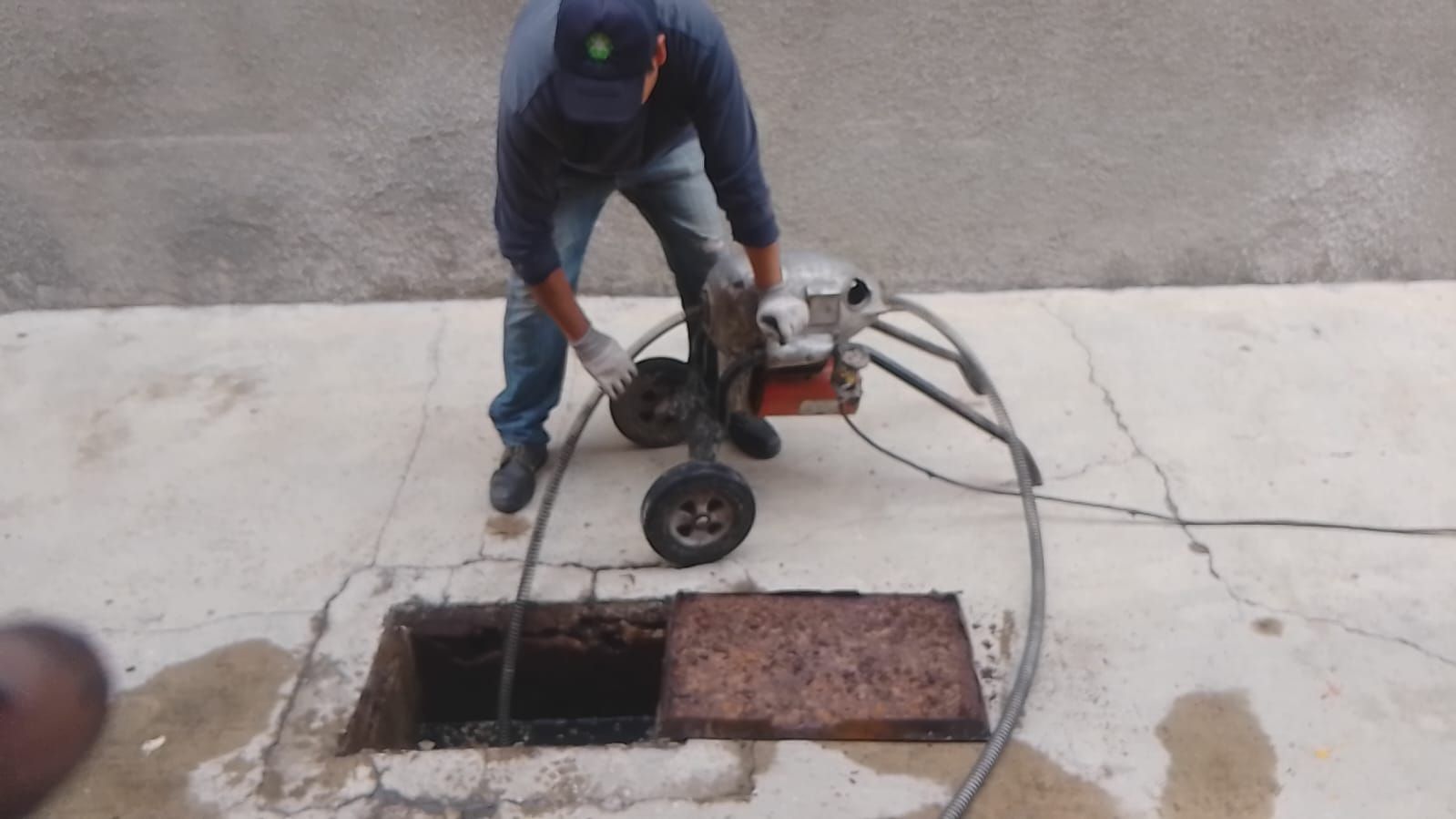 Hombre utilizando una máquina para limpiar una alcantarilla. Asentamiento de hormigón, alcantarilla oscura, herramienta con ruedas.