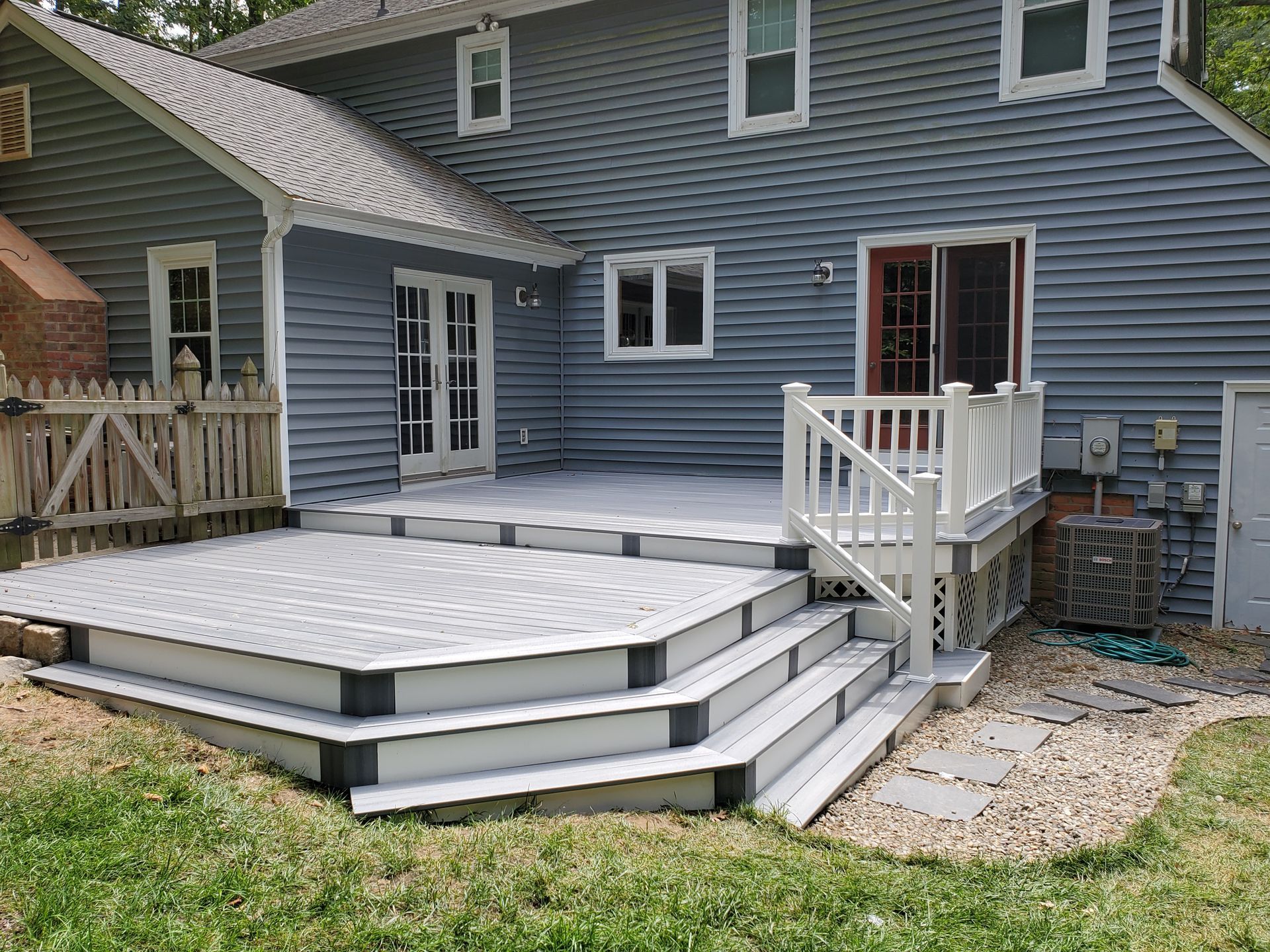 A gray house with a white deck and stairs in front of it.