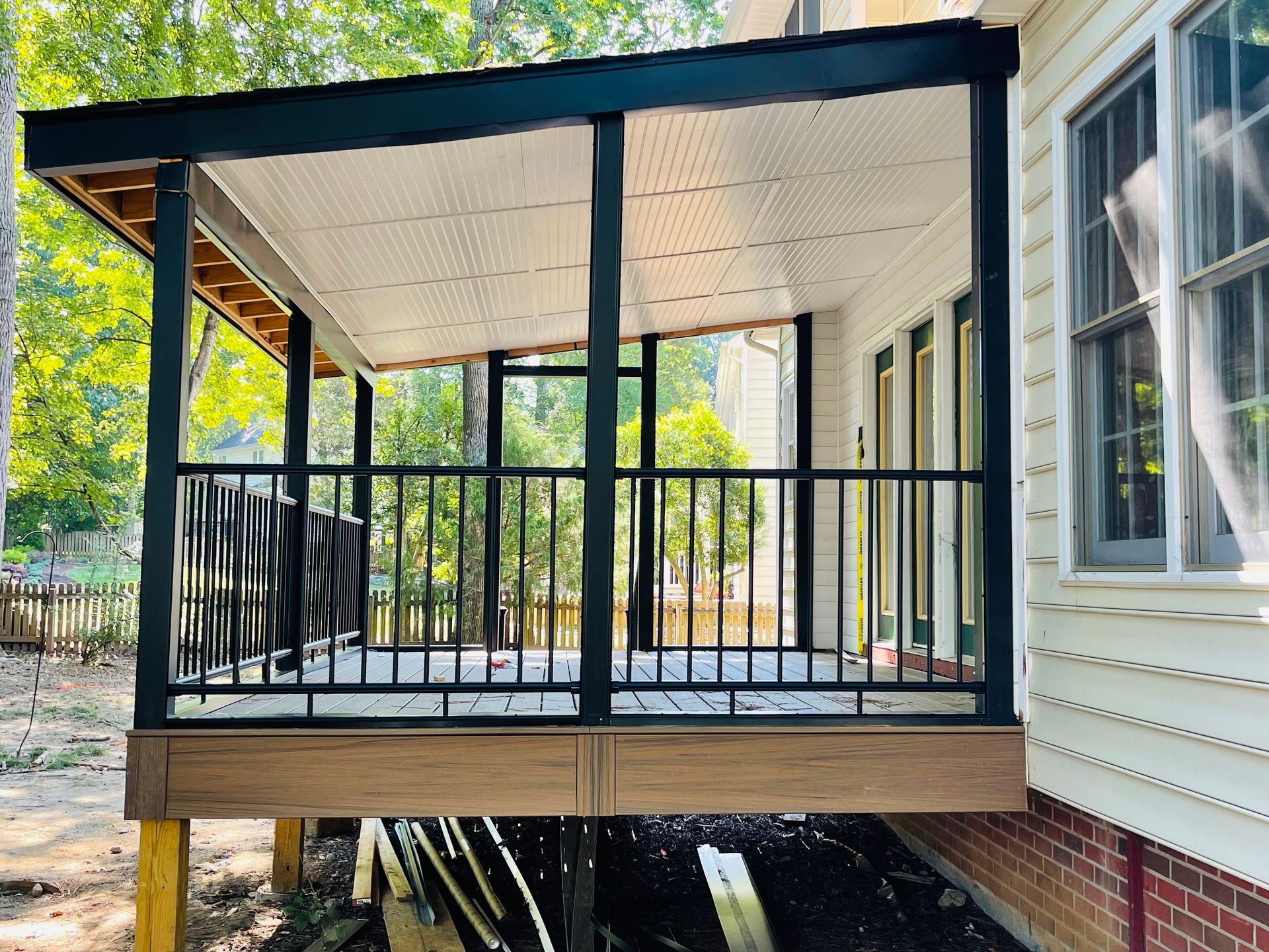 A screened in porch with a black railing on the side of a house.