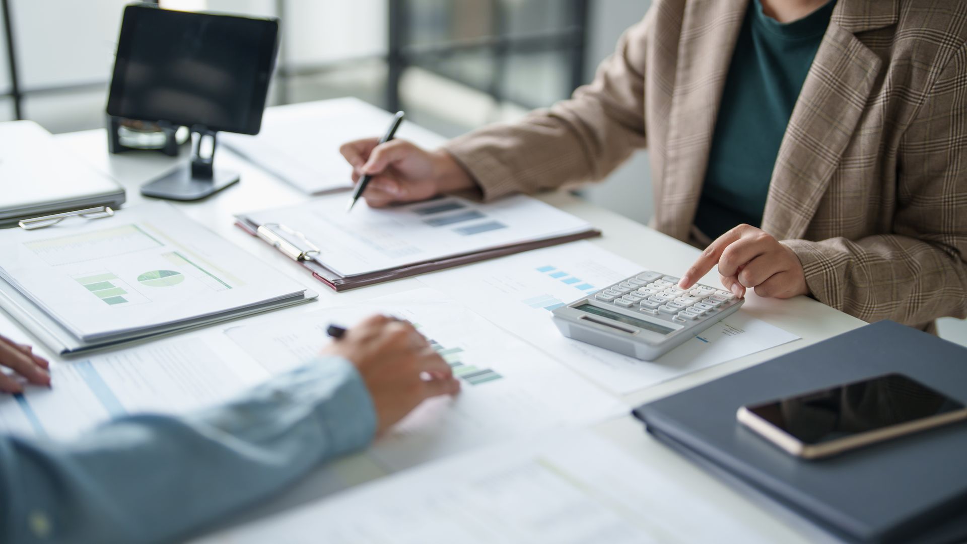 Two people are sitting at a table with a calculator and a pen.