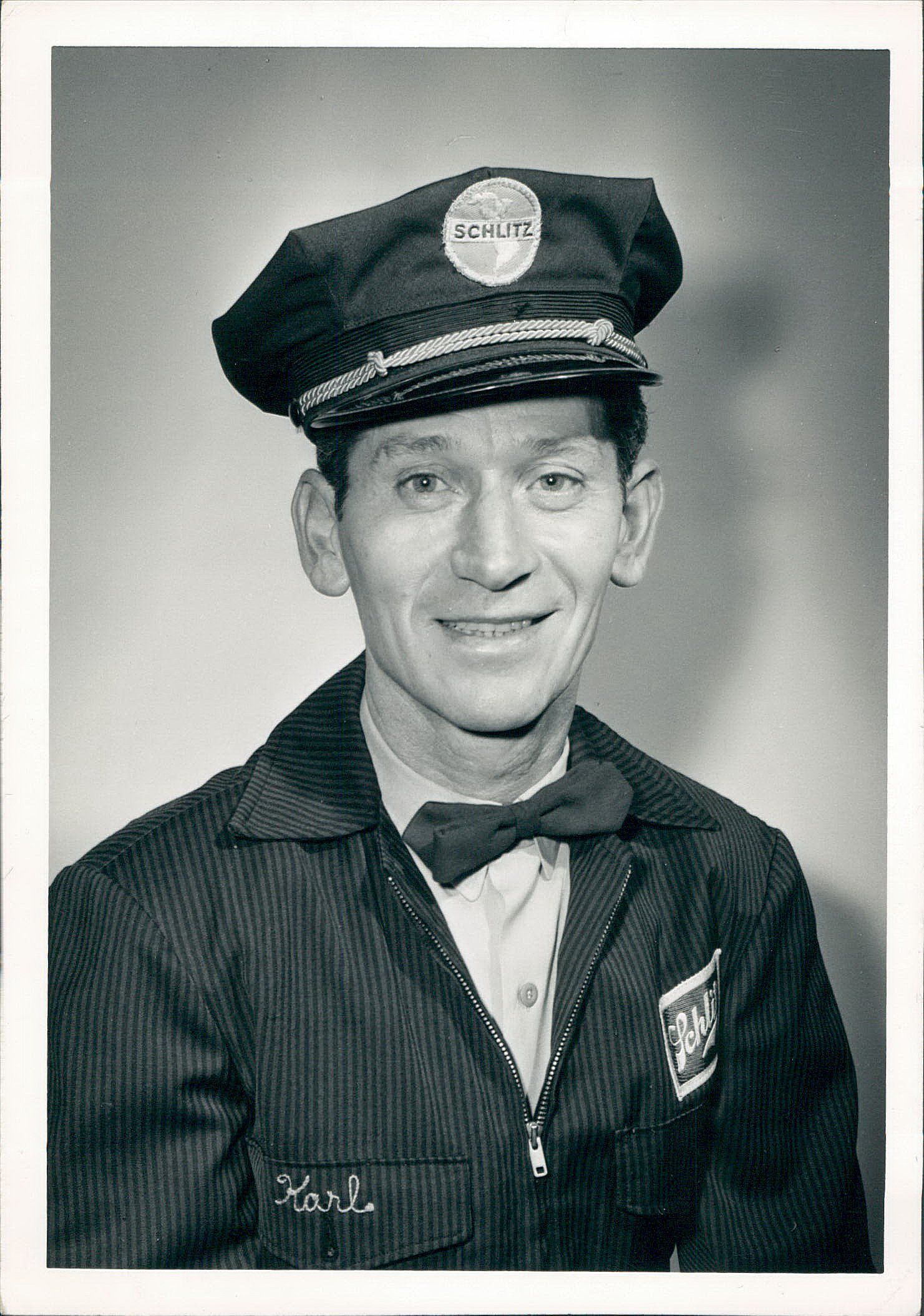 A black and white photo of a man wearing a hat and bow tie.